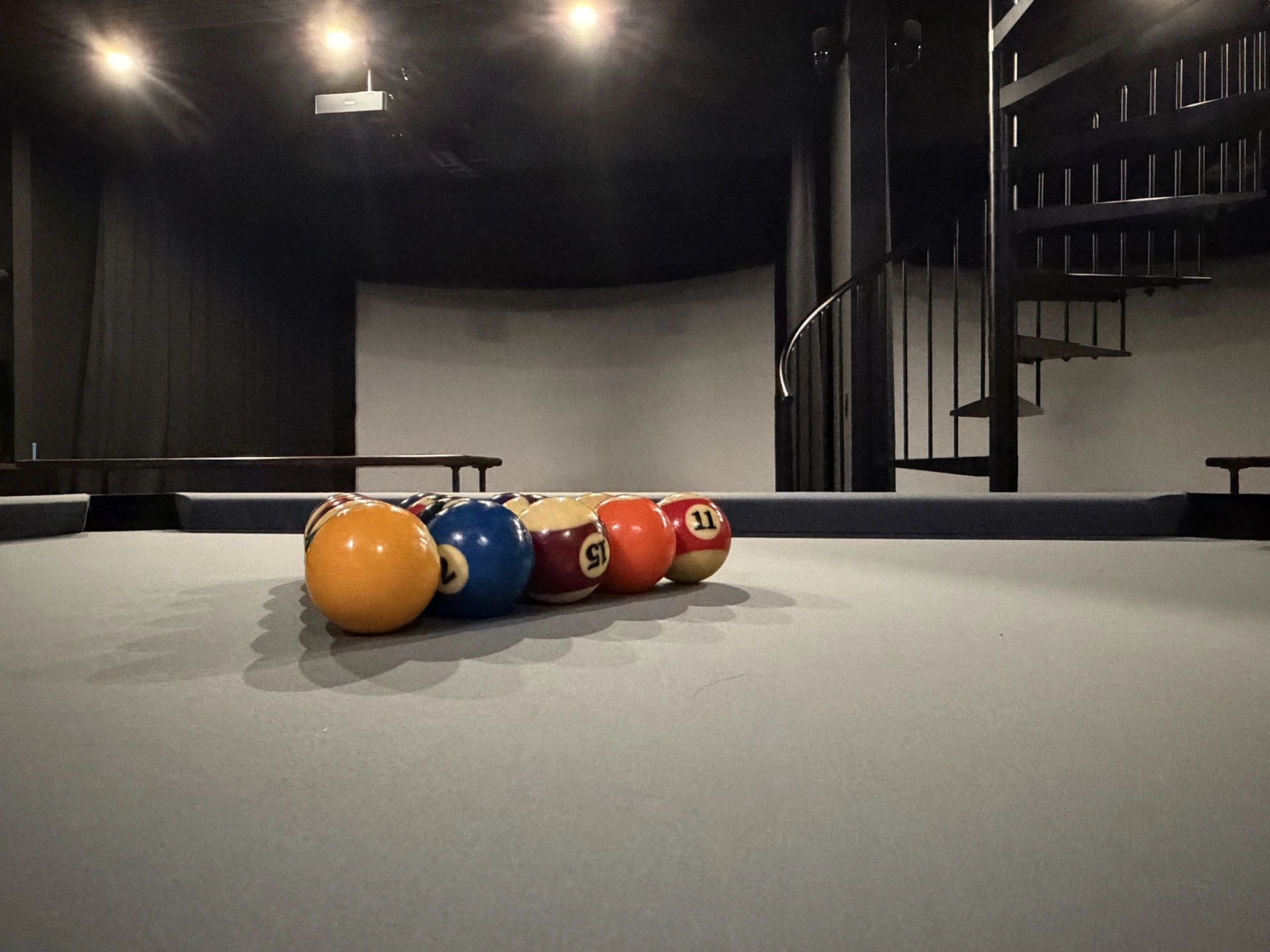 Billiard balls on the table with a golf simulator bay behind them